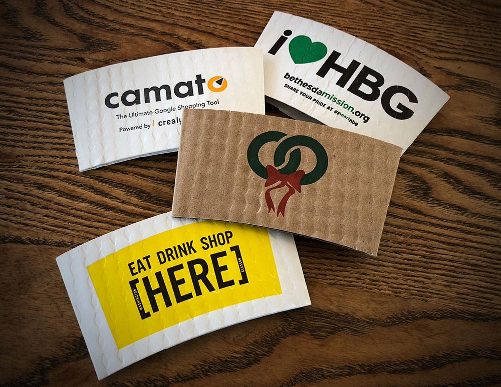 Assortment of Printed coffee cup sleeves printed on white and kraft sleeves with two colors on front and one color on back placed on a tabletop