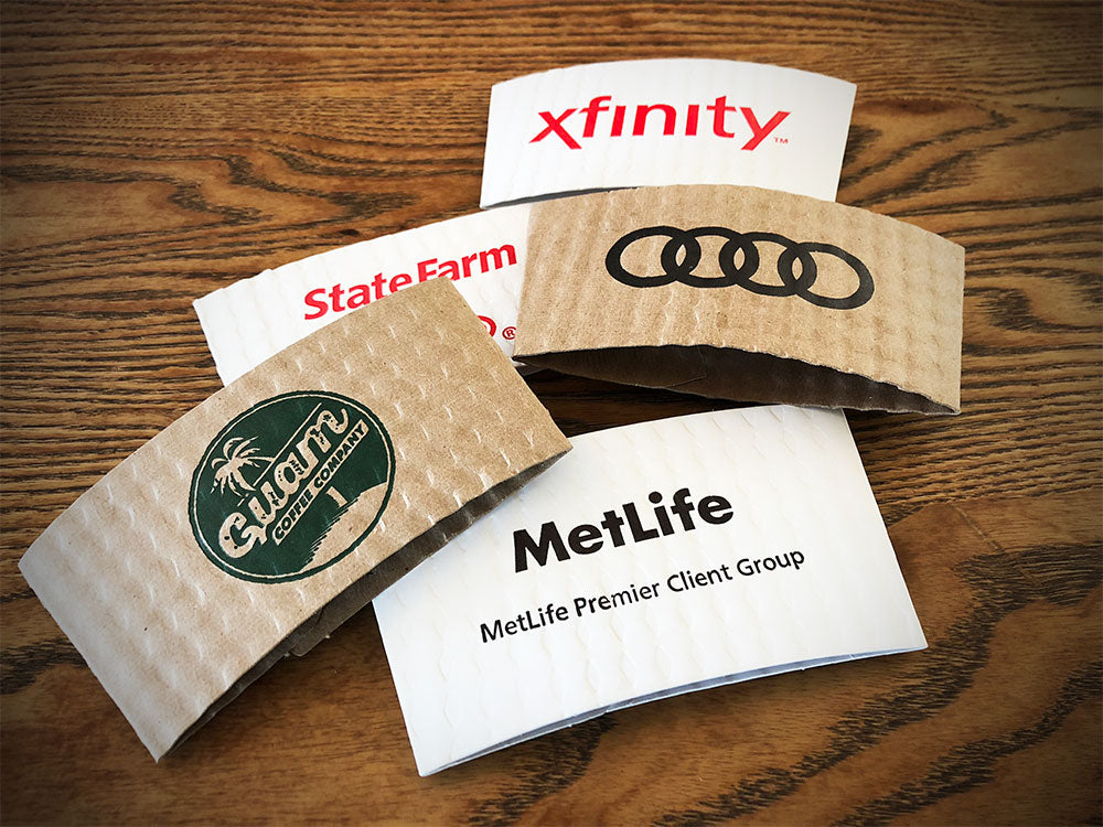 Assortment of custom printed coffee cup sleeves printed using kraft & white sleeves displayed on a wooden tabletop