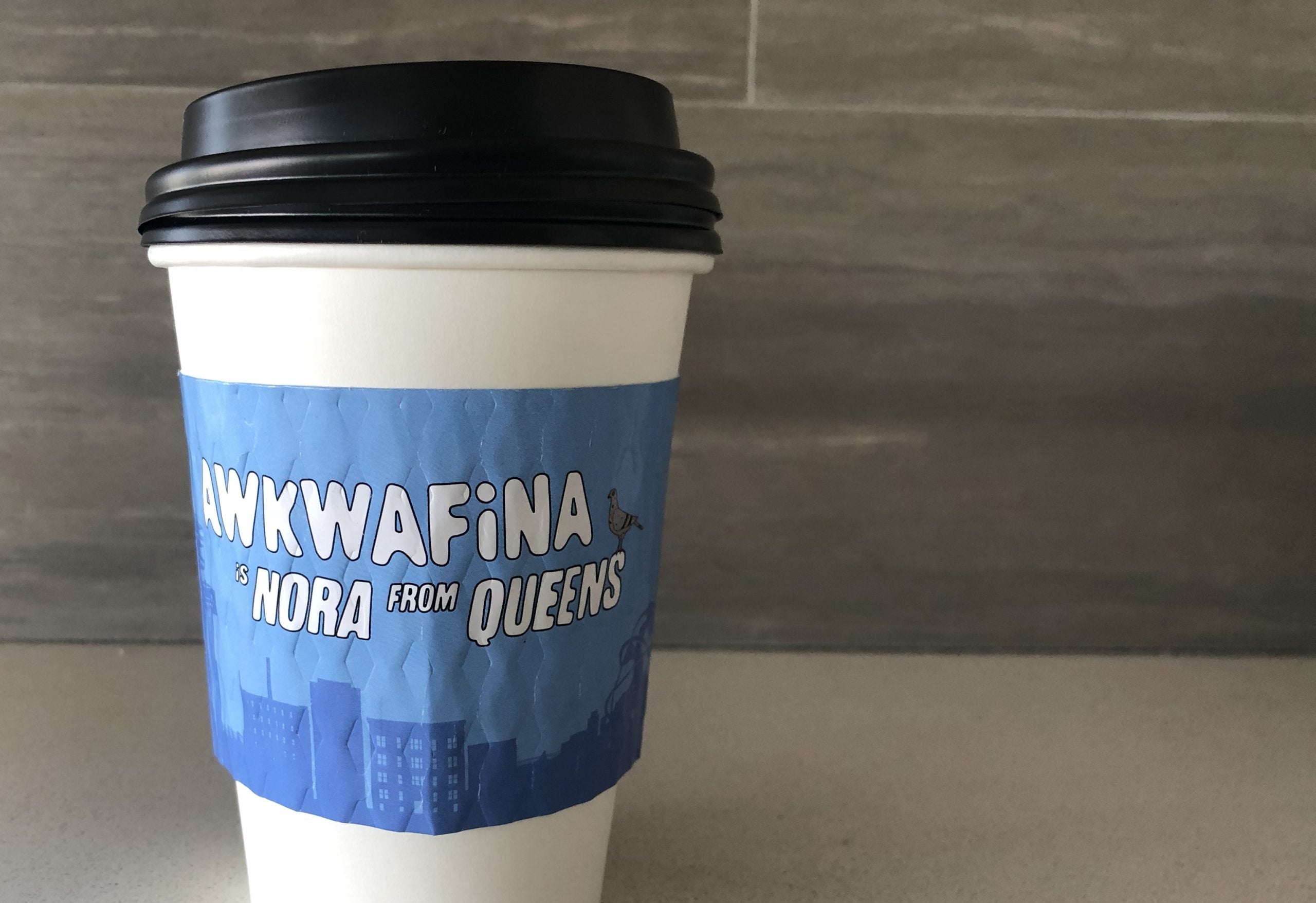 Custom cup sleeves printed in full color for Awkwafina placed on a white paper cup placed on a countertop