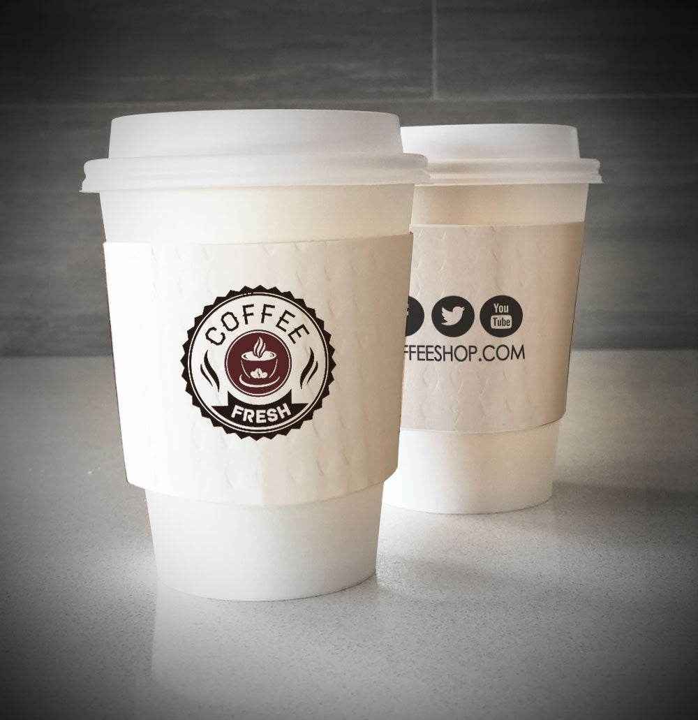 Printed coffee cup sleeves printed on white cup sleeves with two colors on front and one color on back placed on 2 white paper cups placed on tabletop cups.