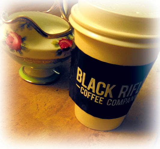 A unique advertising idea is our cup sleeve printed in full color for Black Riffle coffee placed on a white paper cup placed on a countertop