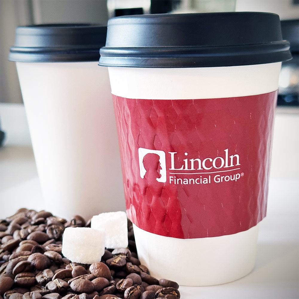 Custom printed coffee cup sleeves printed in full color for Lincoln Financial placed on 2 white paper cups placed on a tabletop along with coffee beans scattered
