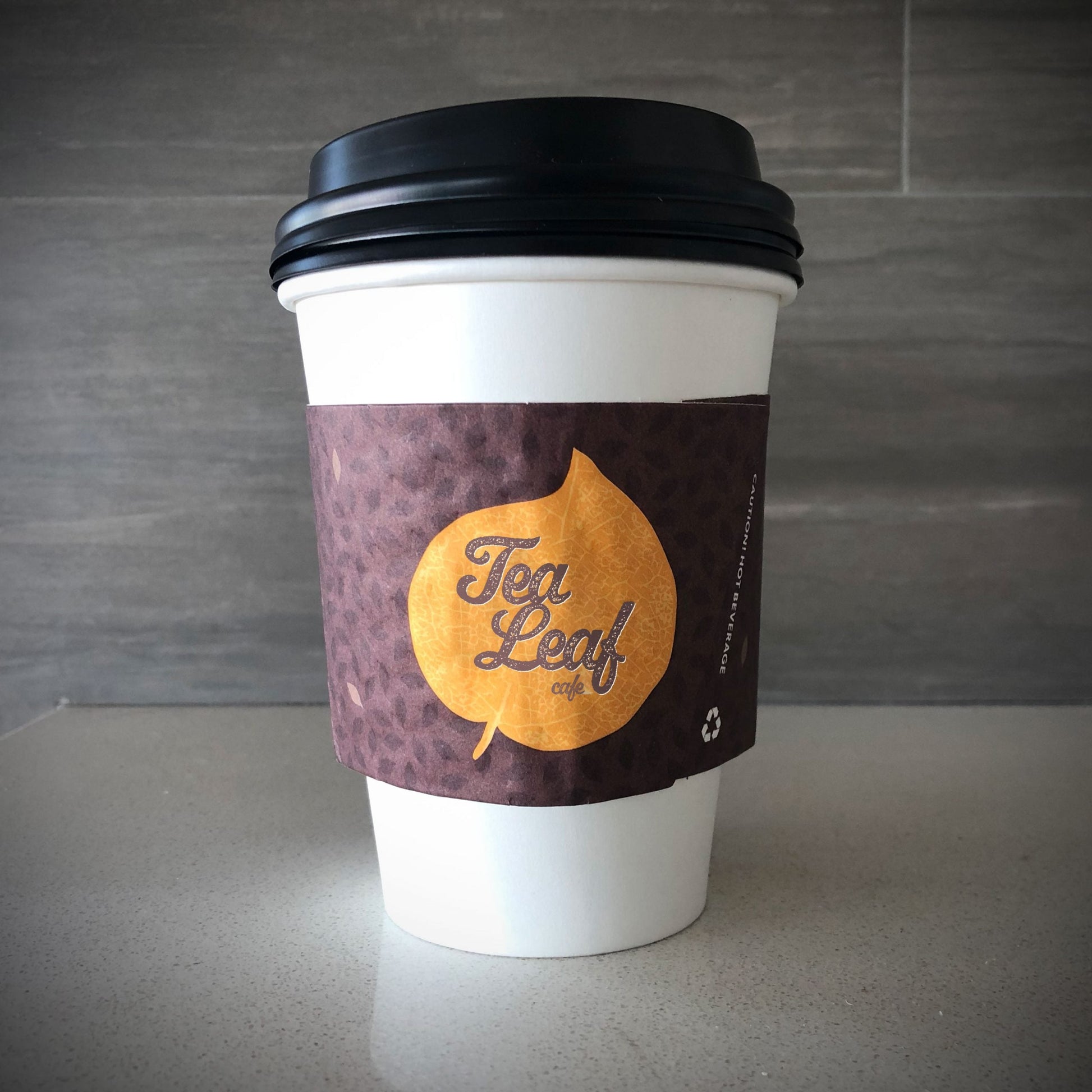Custom printed coffee cup sleeves printed in full color placed on a white paper cup placed on countertop