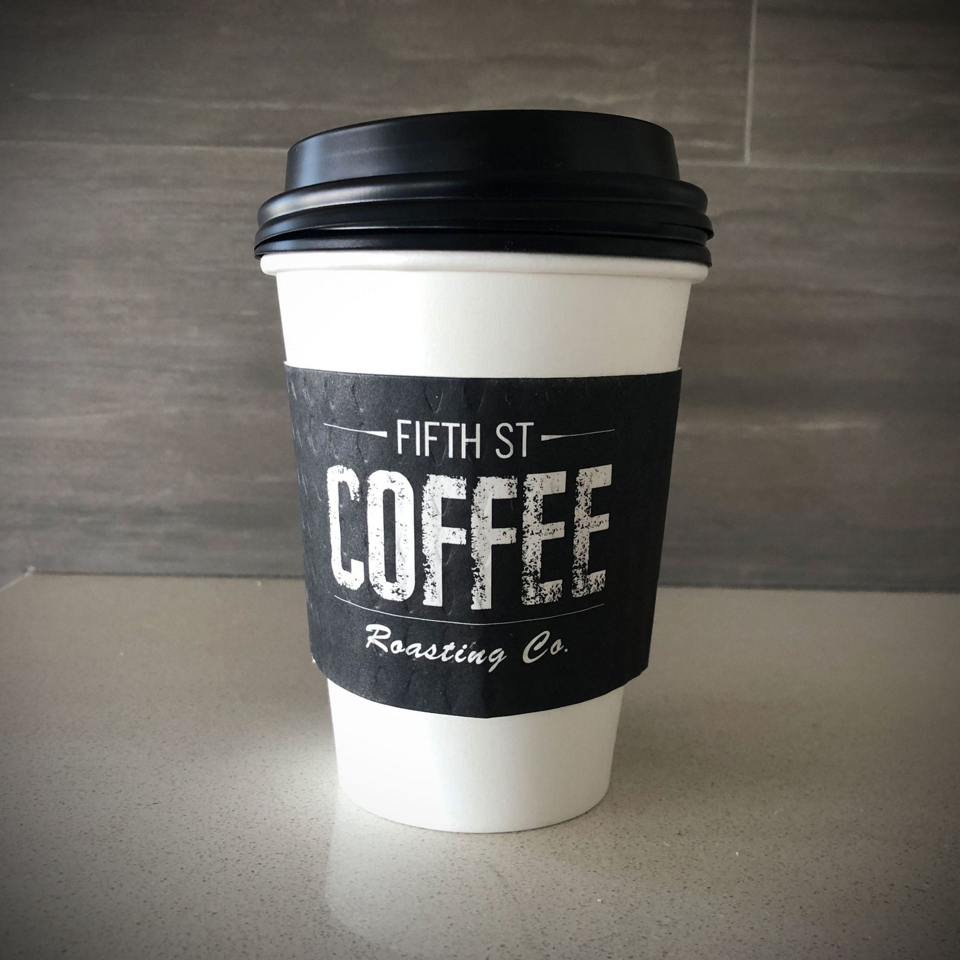 Custom printed coffee cup sleeves printed in full color placed on a white paper cup place on a countertop 