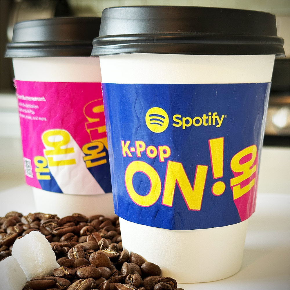 Custom printed coffee cup sleeves placed on white paper cups with coffee beans scattered on the countertop