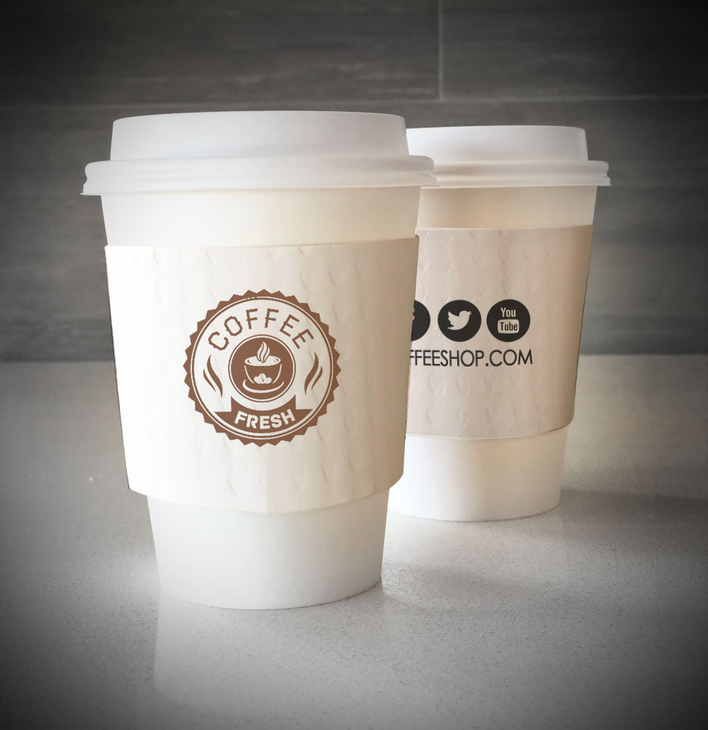 Printed coffee cup sleeves printed on white sleeves with one color on front and one color on back placed on 2 white paper cups that are sitting on a countertop