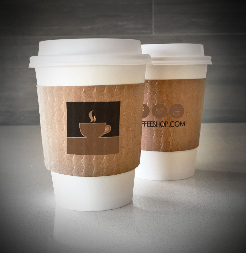 Kraft custom printed cup sleeves printed on both sides with colors of ink placed on 2 white paper cups placed on a countertop