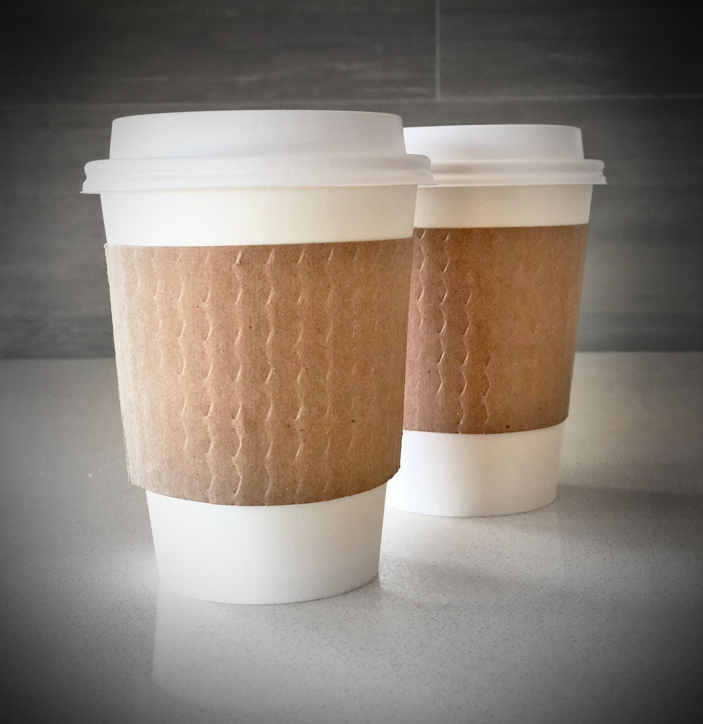 kraft blank coffee cup sleeves placed on 2 white paper cups and are placed on a countertop